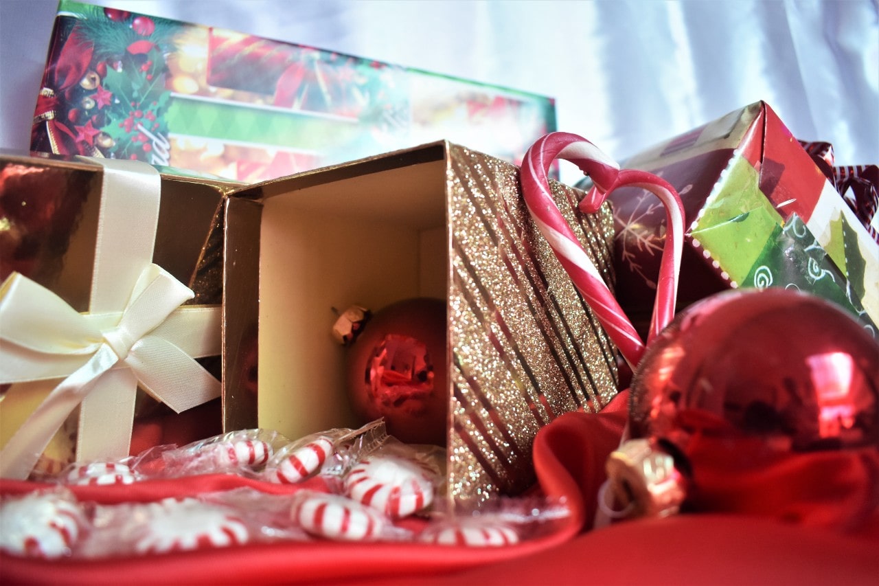 A close-up of an overturned gift box with an ornament inside, among candy canes, pepperminds, and other gifts.