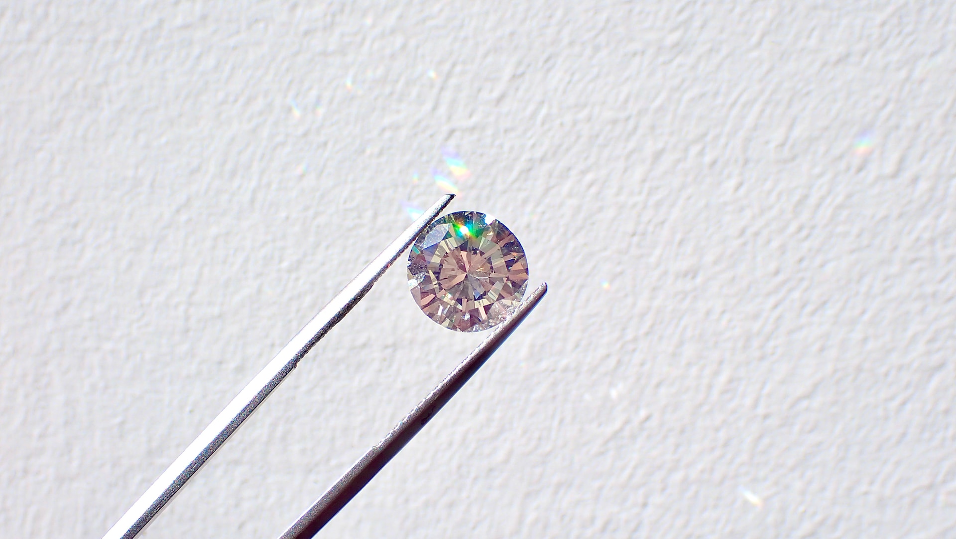 A single round cut diamond being held up to the light by jeweler tweezers