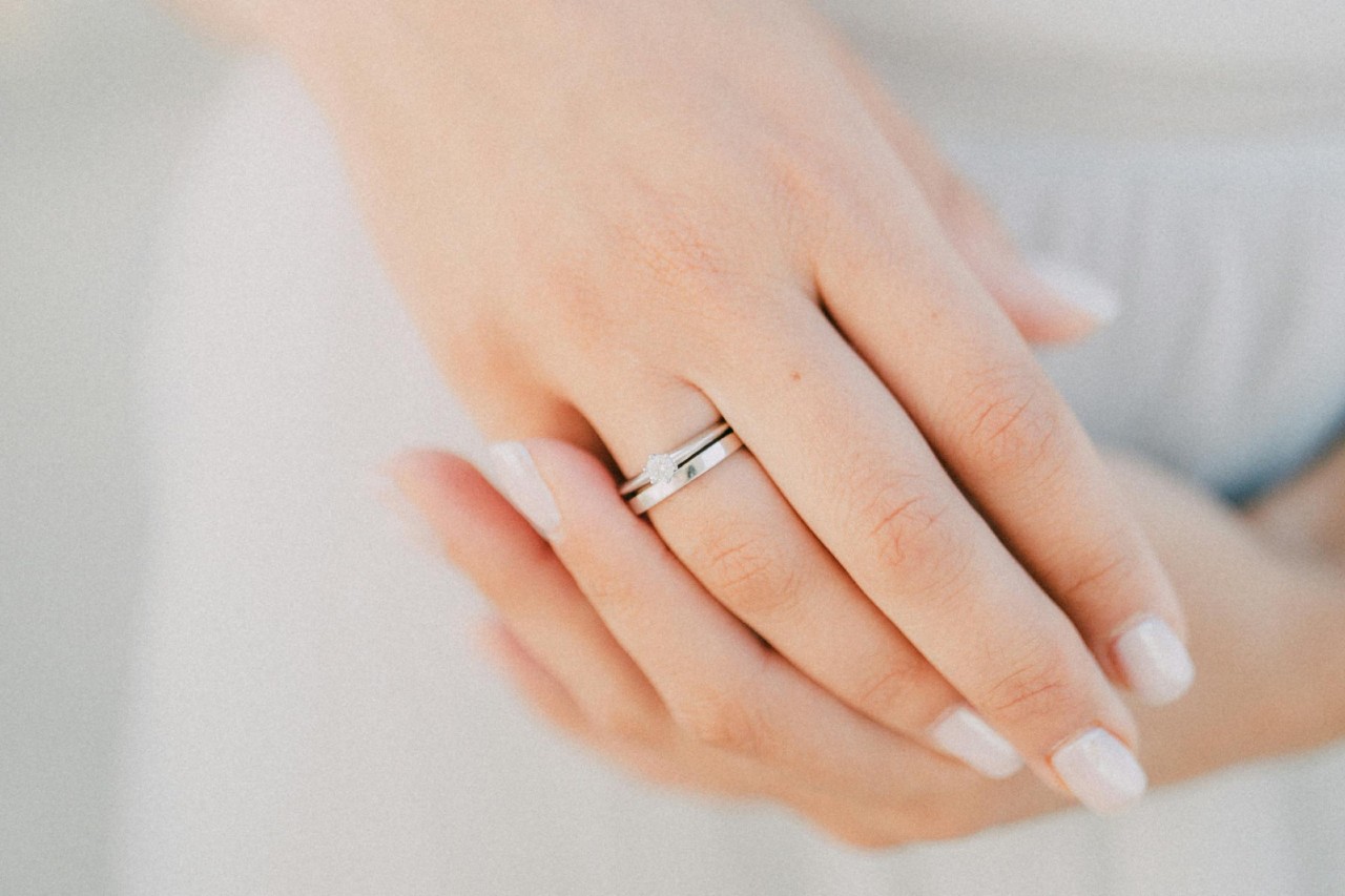 a bride’s hands, one of which is adorned with a diamond engagement ring and wedding band