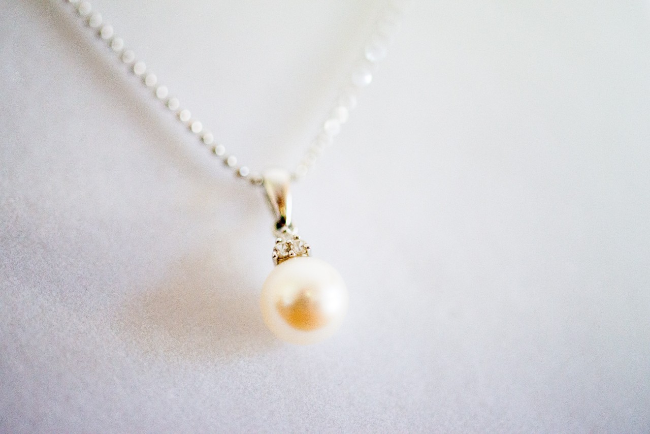 A close-up of a delicate pearl pendant necklace on a soft white backdrop.