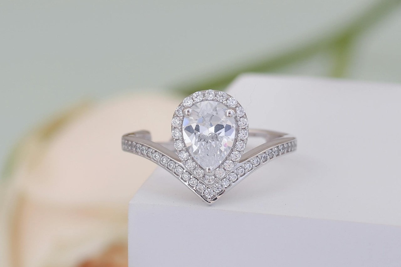 a pear-shaped halo ring sits on the edge of a white box.