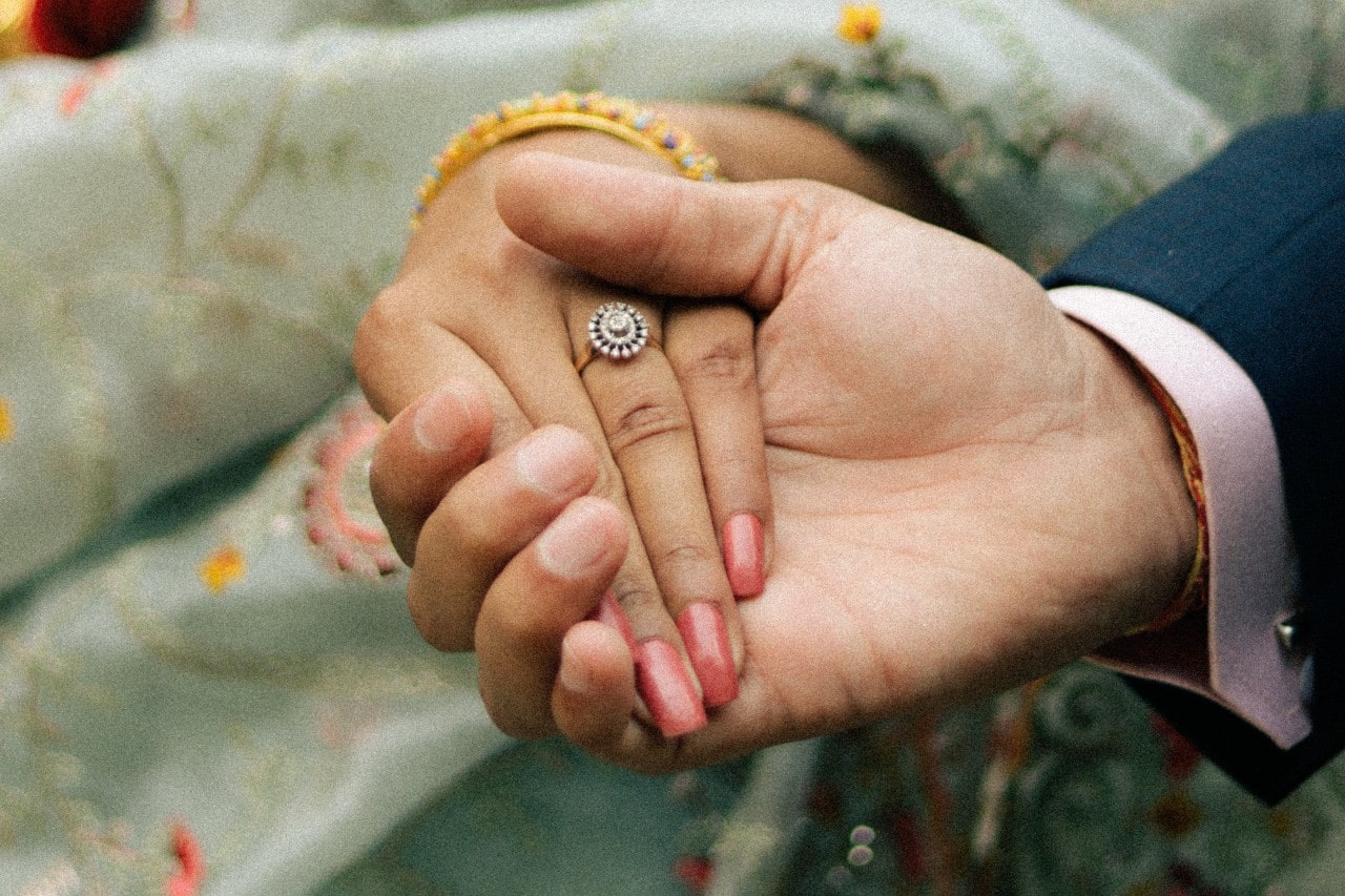 a halo ring on a woman’s hand as she holds her fiance’s hand.