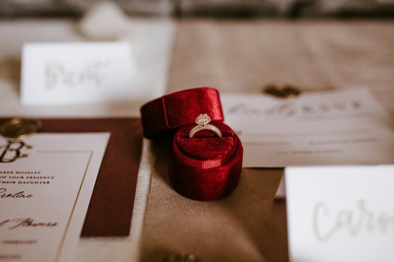 a ring sits in a red ring box among wedding invitations and labels.