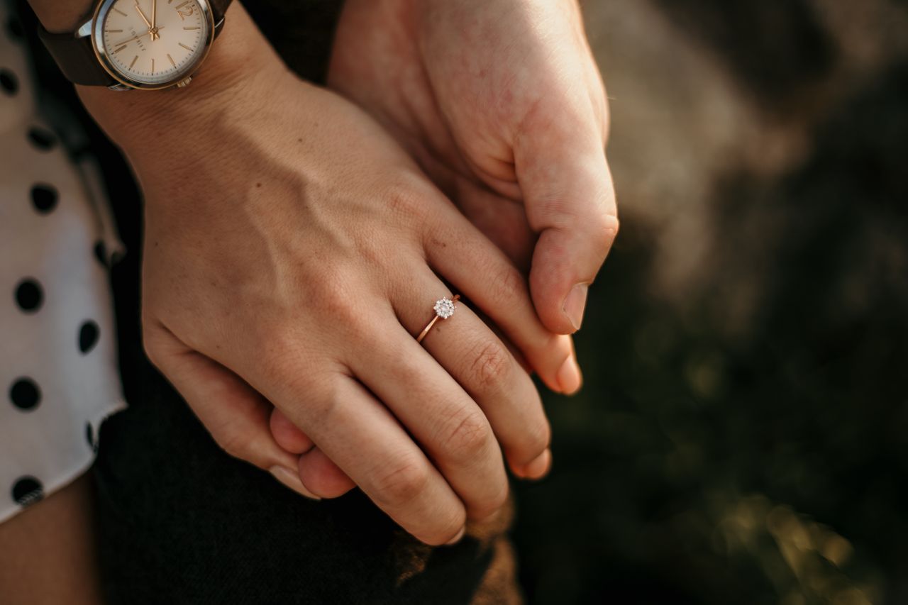 Simple diamond engagement ring from Brockhaus Jewelry on a woman's hand as she holds hands with her love.