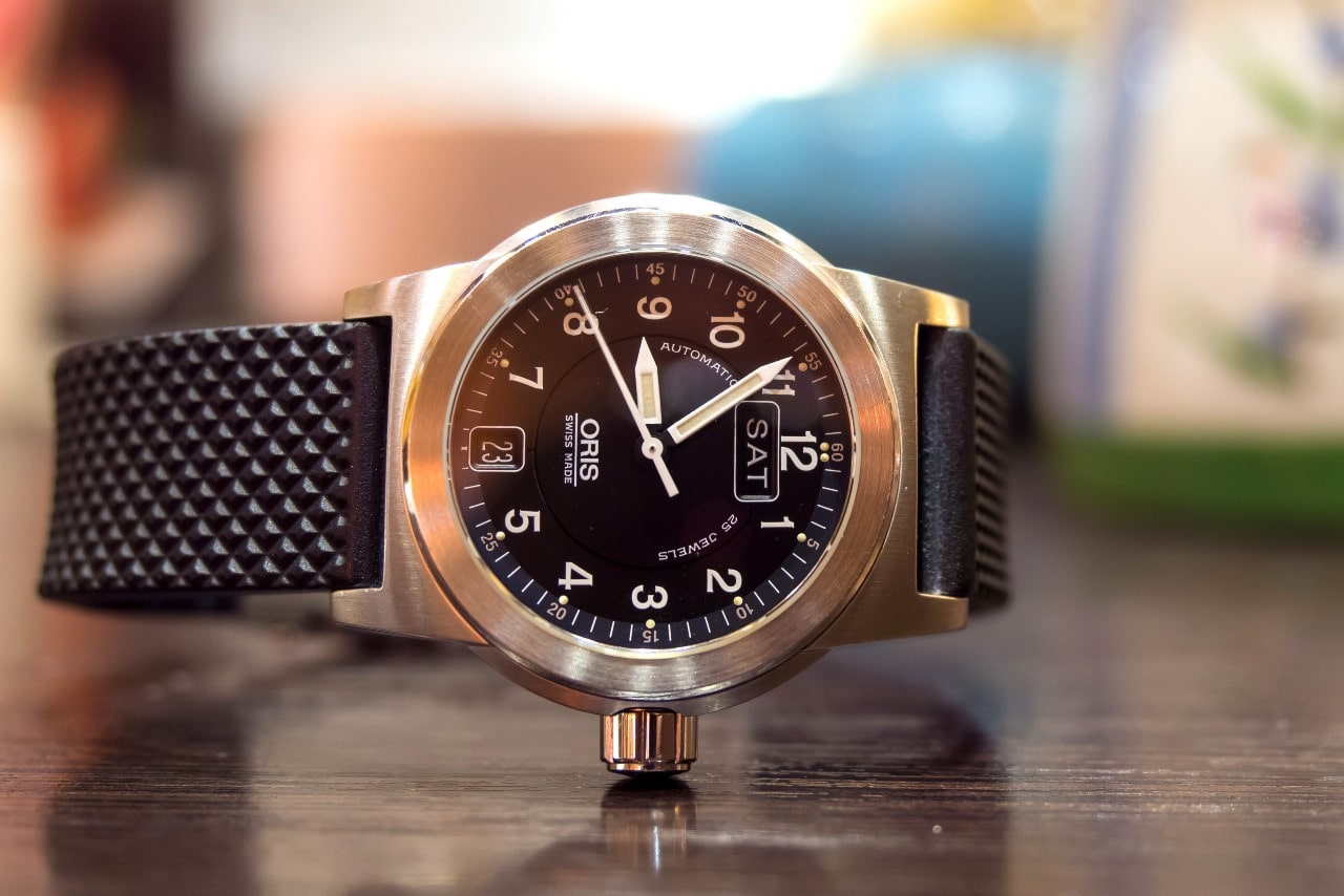 A close-up of an Oris watch, displayed on its side on a wooden table.