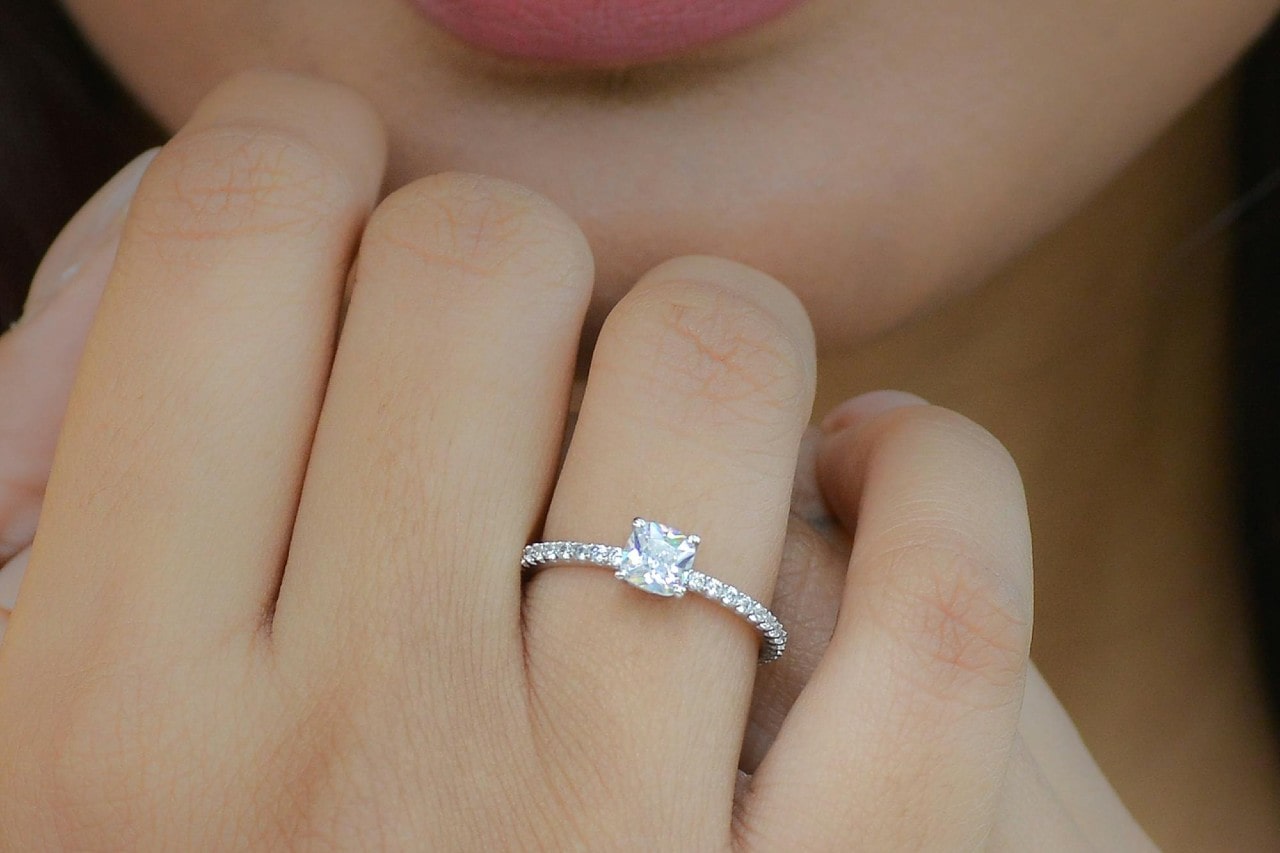 a woman’s hand held close to her face, wearing a side stone engagement ring
