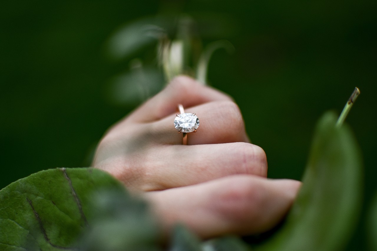 a woman’s hand wearing a solitaire engagement ring and holding stems