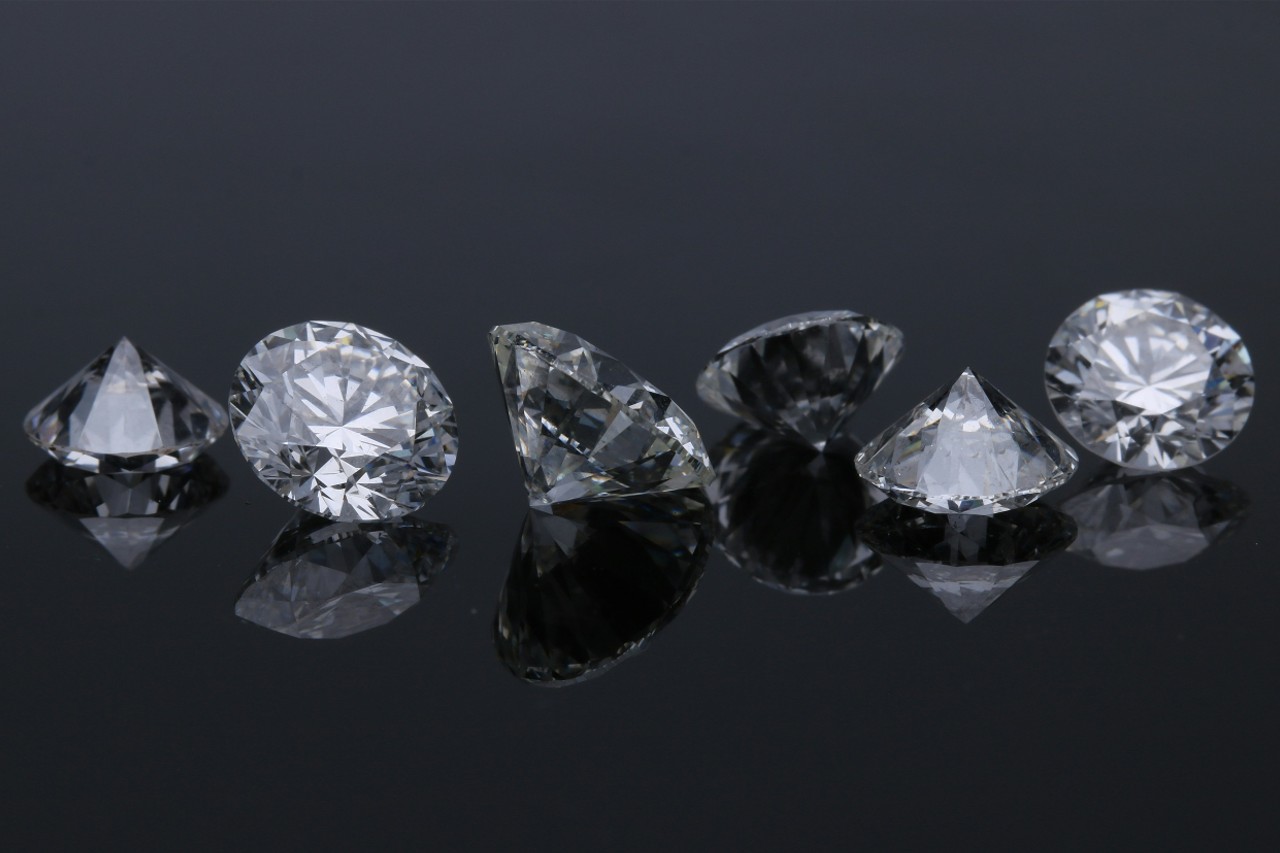 A close-up of six round cut diamonds displayed side-by-side on a dark backdrop.