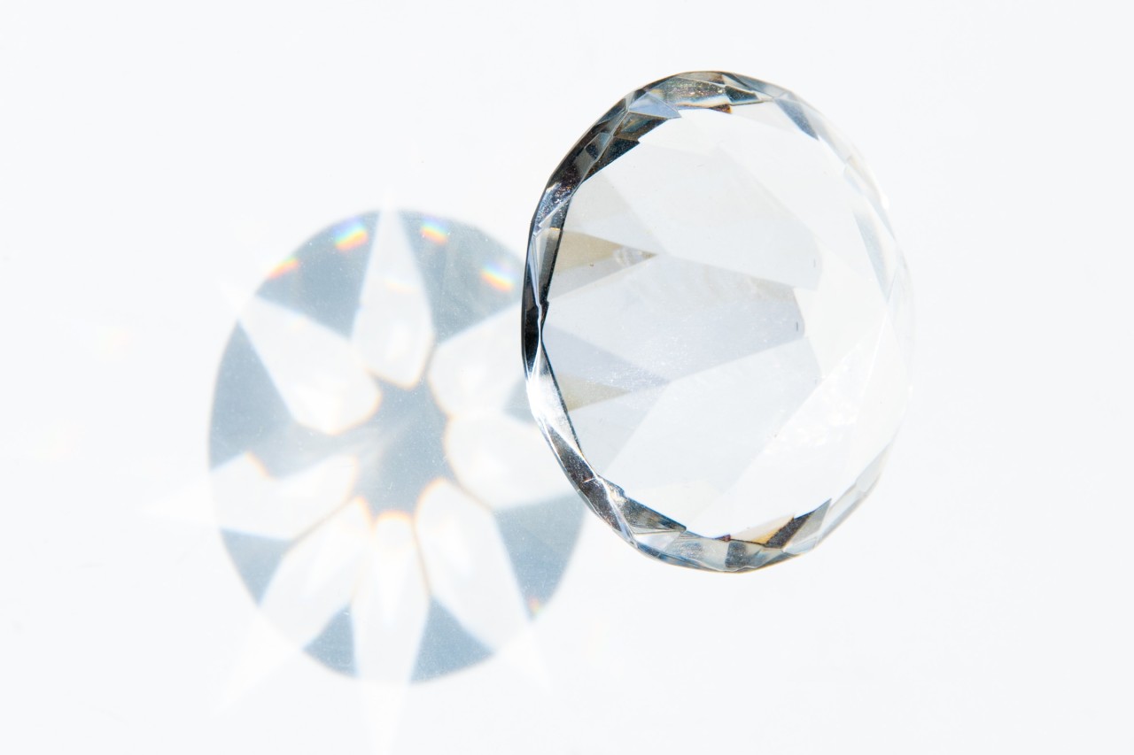 A close-up of a glistening diamond casting light reflections on a pale background.