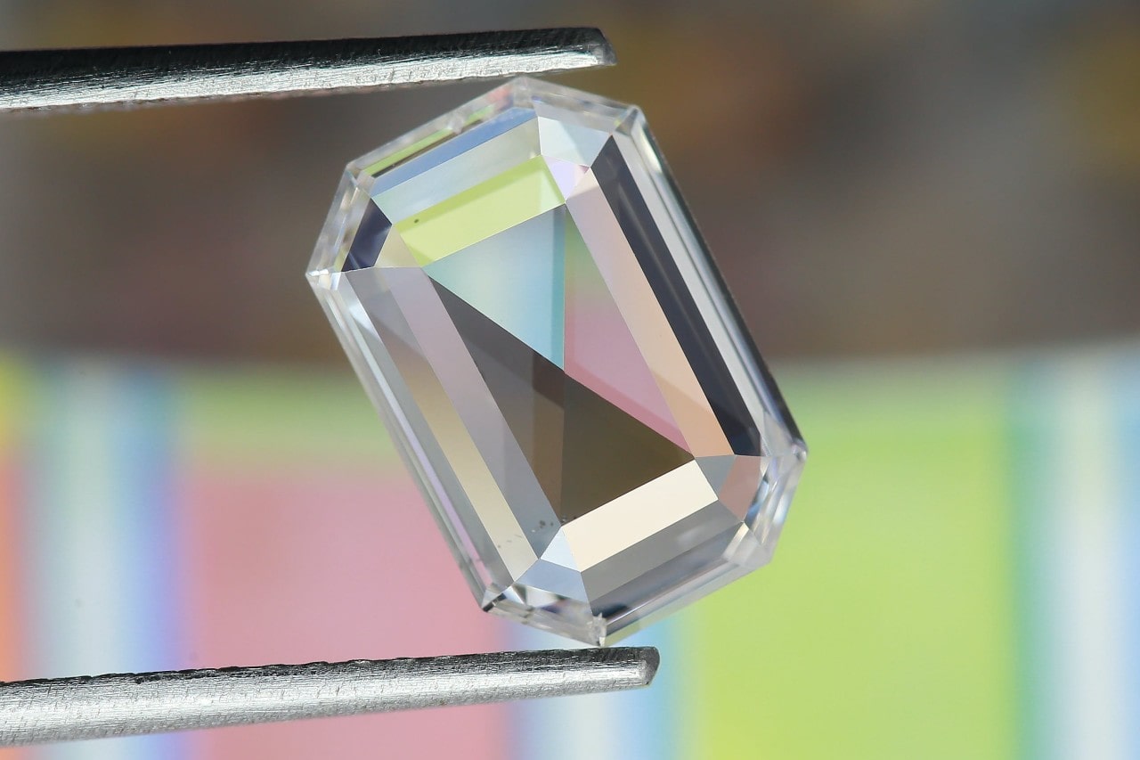 A close-up of a stunning diamond held in jeweler’s tweezers, reflecting the colorful background in its facets.