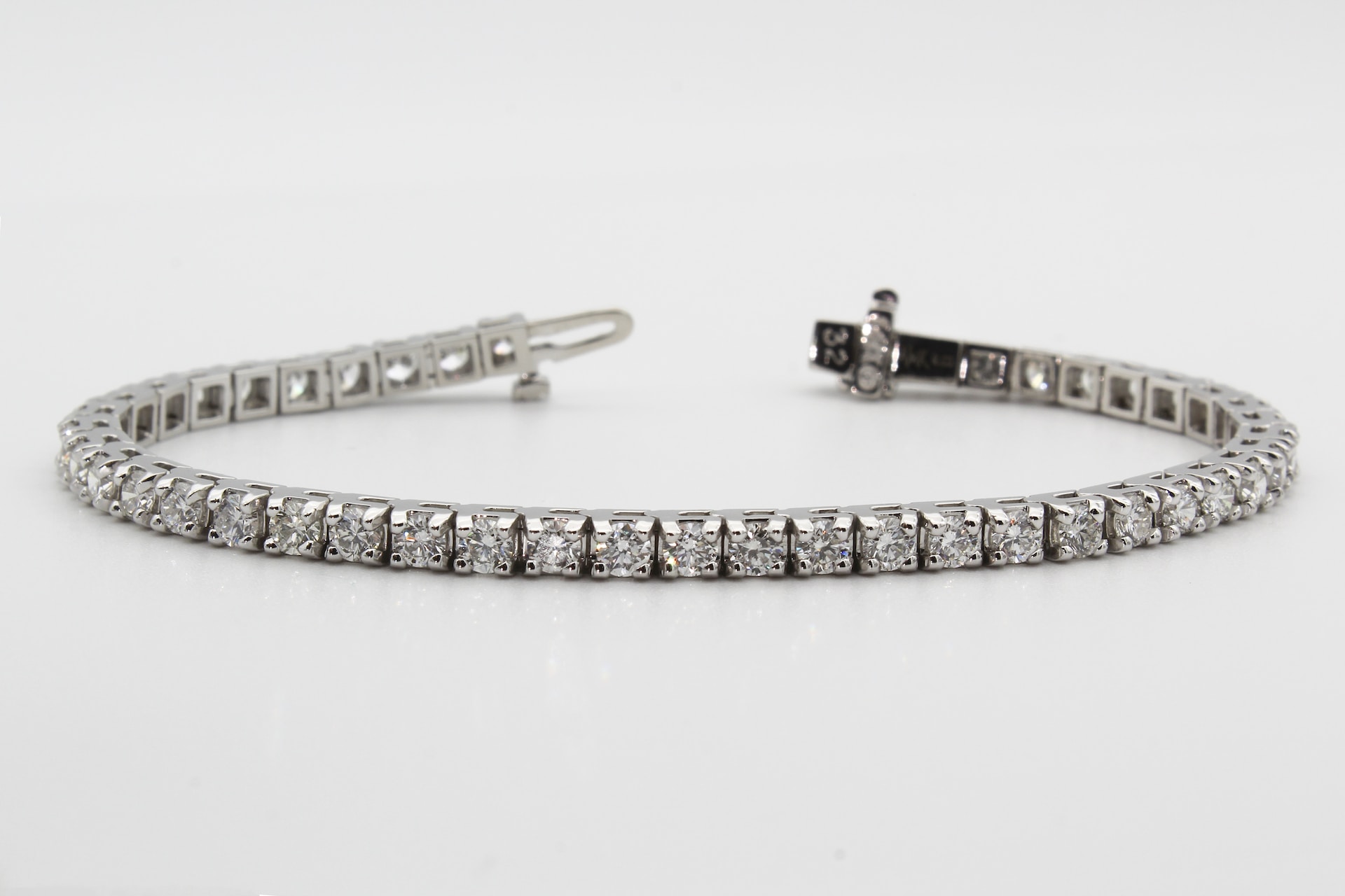 a white gold diamond tennis bracelet with prong set diamonds on a white surface