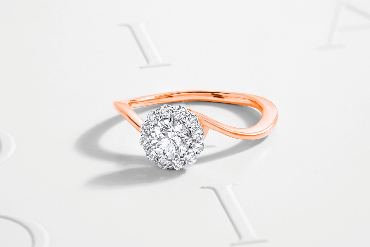 A close-up of a delicate engagement ring with a rose gold band.