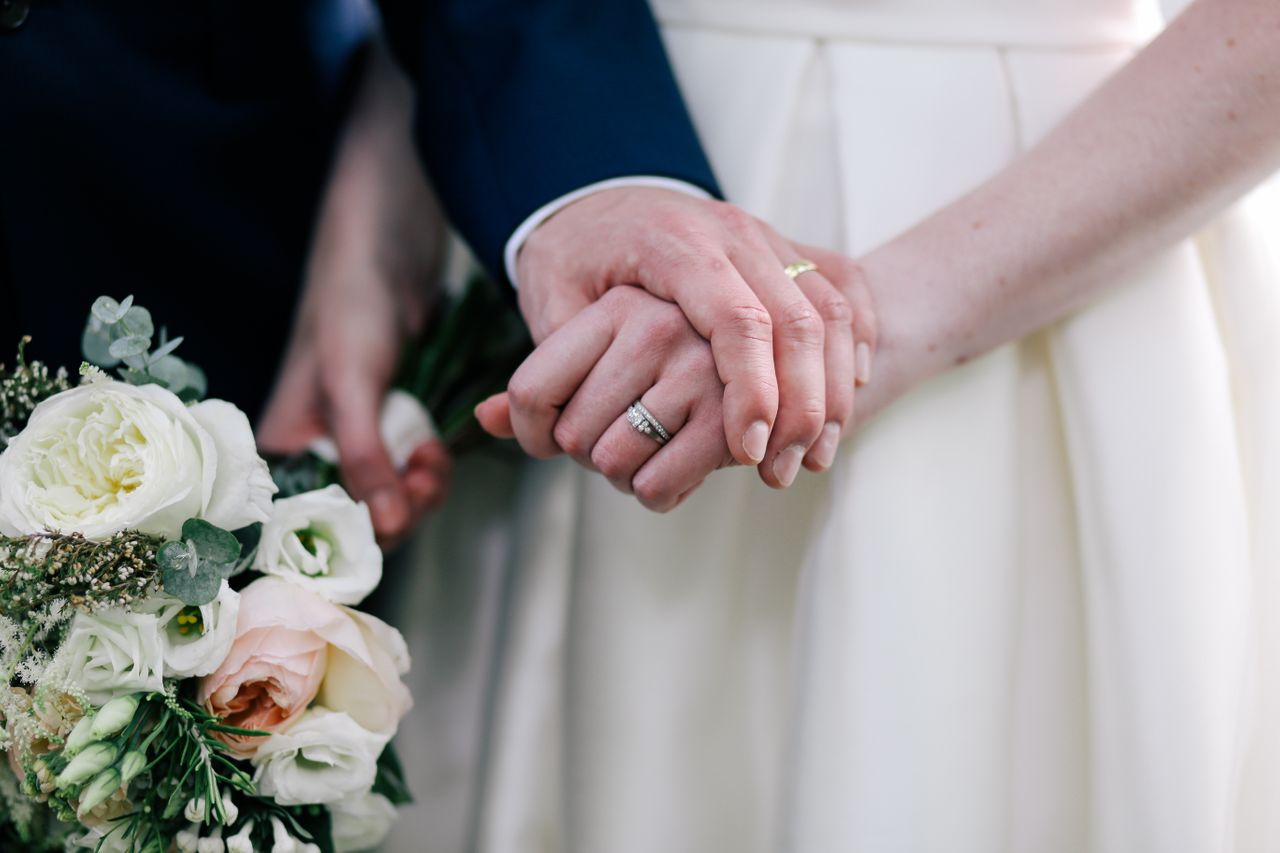 A close-up of a bride and groom’s hands at the altar, wearing their wedding bands.