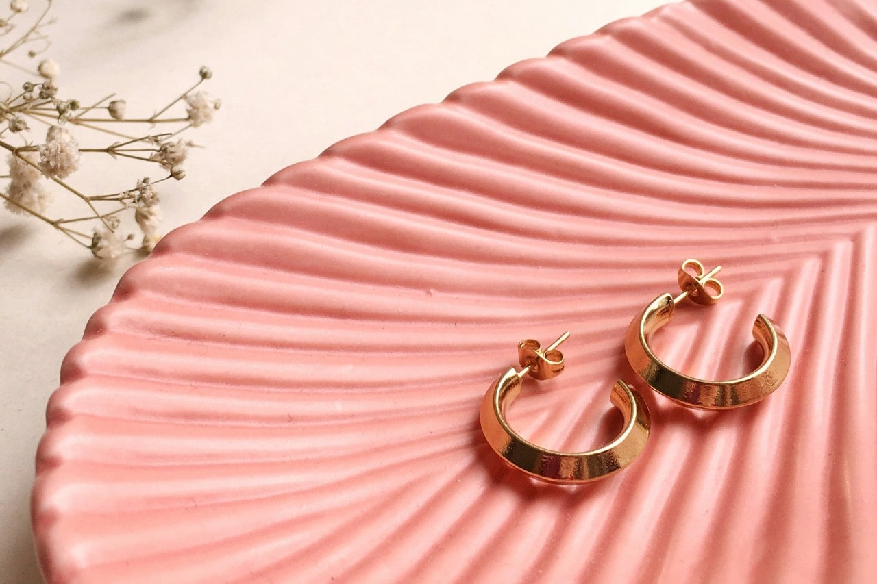 A close-up of a pair of gold earrings on a decorative tray.