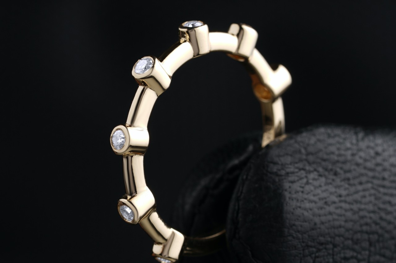 a yellow gold bezel set diamond band held between gloved fingers