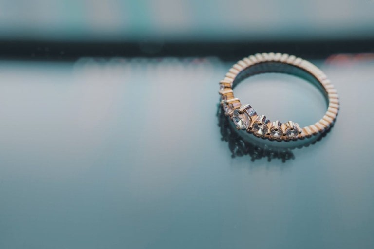 A yellow-gold wedding band with an array of prong-set lab-grown diamonds sits alone on a reflective surface.