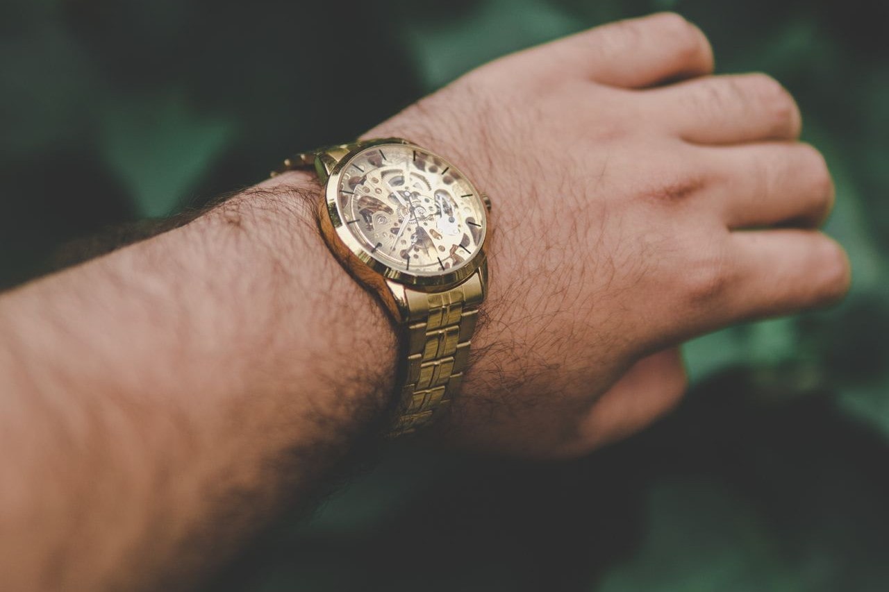 men's gold watch on hand with green leaves in background