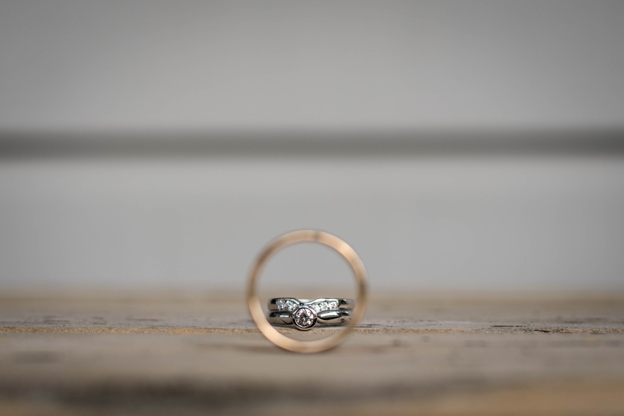 A close-up of a bridal stack viewed through a men’s wedding band.